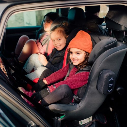 3 niños sentados en una fila de asientos en la silla a contramarcha Axkid Minikid 4 Pro gracias a su diseño compacto